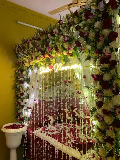 A beautiful 'Welcome Bride' setup with a bed canopy made of flowers and hanging floral strings. A custom neon sign with the couple's names adds a personal and modern touch.