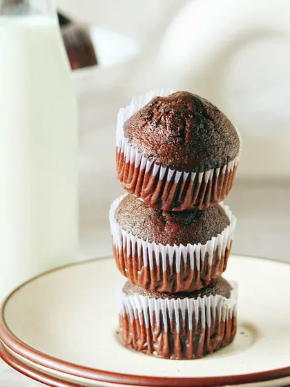 A simple, clean shot of three stacked chocolate muffins next to a bottle of milk. The bright, white setting gives it a fresh, wholesome, and classic feel.
