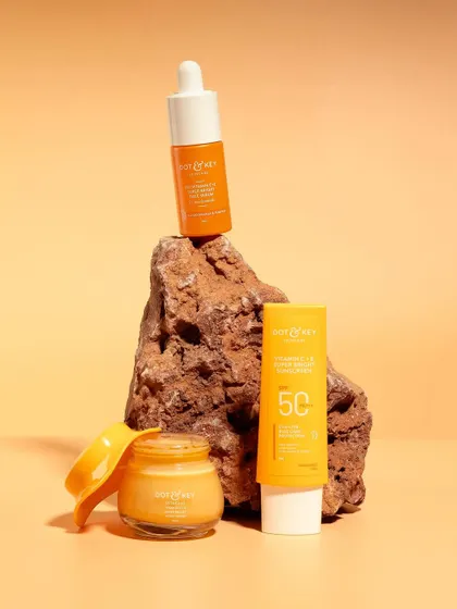 A product family shot for a Vitamin C skincare range. The products are styled on a rock against a warm, sandy-colored background, giving the line an earthy and natural feel.
