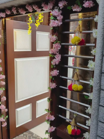 Entrance decoration using artificial pink flower garlands. This creates a soft and welcoming entryway for any festive or religious occasion at home.