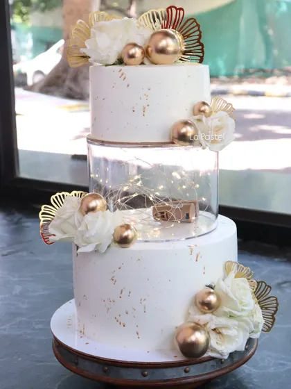 I love adding a little bit of drama with fairy lights! This three-tier white and gold wedding cake has a clear separator tier filled with twinkling lights, decorated with white peonies and gold accents for a magical touch.