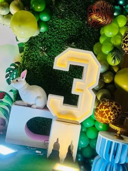 A light-up marquee number "3" integrated into the jungle decor, surrounded by green balloons and a rabbit prop.