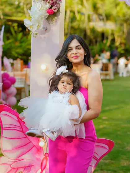A beautiful mother and daughter portrait from a butterfly themed birthday party. The birthday girl looks adorable in her white dress, posing with her mom in front of the themed decor.