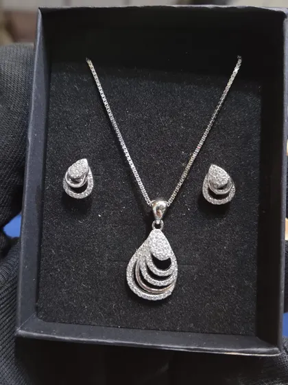 A close-up of a 925 silver chain and pendant set with matching earrings. This layered teardrop design is elegant and modern.
