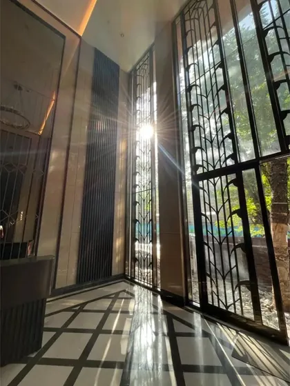 Sunlight streams through the tall, ornate window screens of a residential lobby in Mumbai. This design element not only adds security and privacy but also creates beautiful, shifting patterns of light within the entrance space.