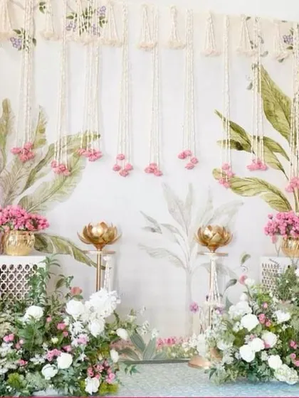 A soft and elegant backdrop with a painted leaf design. The hanging strings of jasmine and pink flowers, combined with floral arrangements, create a romantic and delicate setting.