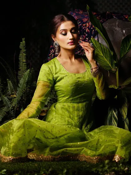 A serene, seated portrait in a lush green setting. The lighting is soft and focused, highlighting the model's features and the texture of the dress.