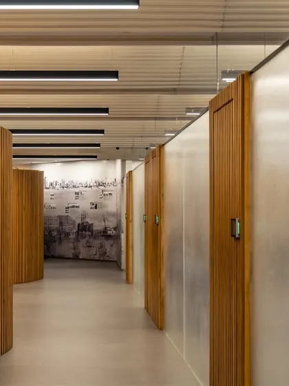 A hallway in the updated UTI HQ features curving, slatted wood partitions that create a rhythmic, sculptural effect while housing private offices.