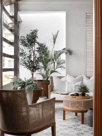To evoke the airy feel of a traditional Kerala home in a compact apartment, we enlarged the windows and styled the balcony with light rattan furniture, plush white cushions, and abundant greenery.