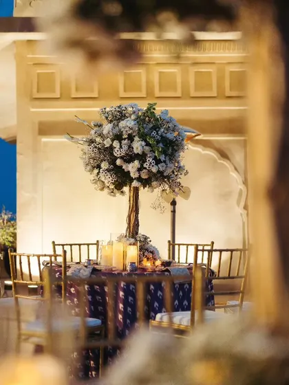 A beautifully styled table centerpiece for the Sufi Night, featuring a tree-like floral arrangement and candles, seen through a soft-focus foreground.