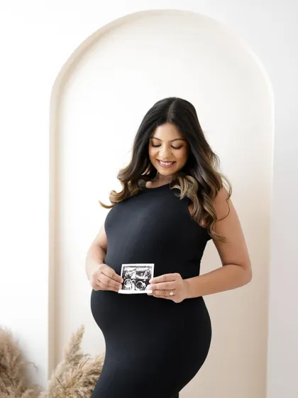 A simple and modern portrait. The mom-to-be holds her sonogram, her black dress and the clean studio background creating a chic and timeless look.