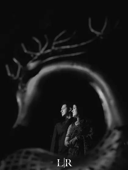 A creative black and white portrait of a couple, framed by the silhouette of a deer sculpture.