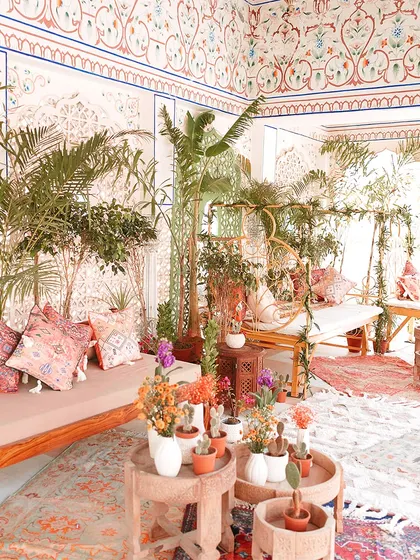 A wide view of a Mehendi lounge, featuring a mix of colorful rugs, plush seating, and abundant greenery. The goal is to create a space that is both beautiful and comfortable.