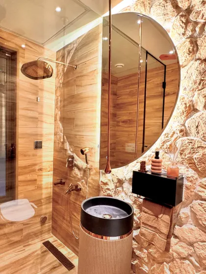This powder room is all about raw luxury. I contrasted a rough, exposed stone wall with smooth, wood-paneled walls and a sleek, round mirror. The cylindrical pedestal sink and rose gold fixtures add a touch of modern elegance, while the integrated steam bath function makes it a true wellness space.