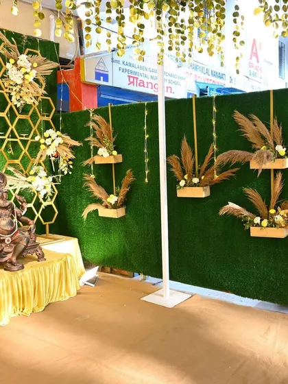 A unique decor element combining a Ganesha idol with a modern backdrop of a green wall and pampas grass arrangements. This blends tradition with contemporary design trends.