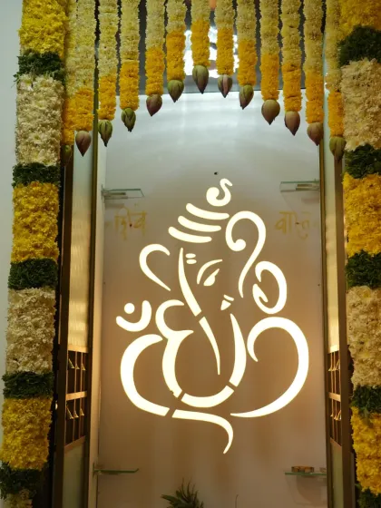 A beautiful entrance to a pooja room for a housewarming, with a backlit Ganesha design on the door framed by marigold garlands.