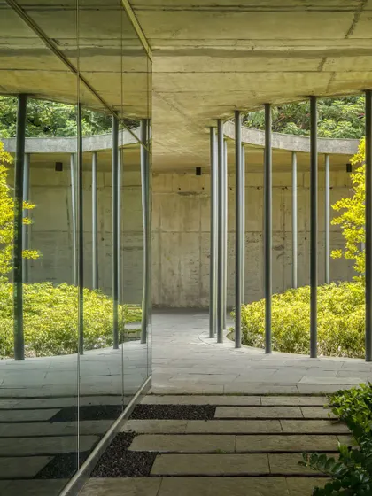 A tranquil corridor at the Vasind Administrative Office, where a glass wall reflects the lush greenery of the courtyard. The design uses reflection and transparency to amplify the presence of nature within the building.
