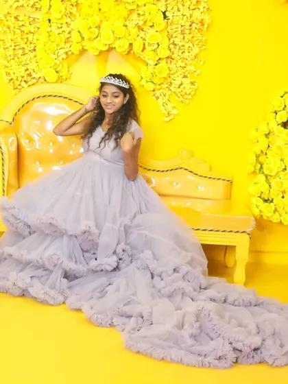 A striking maternity photo with a woman in a light purple gown seated on a yellow vintage-style couch against a matching yellow floral background.