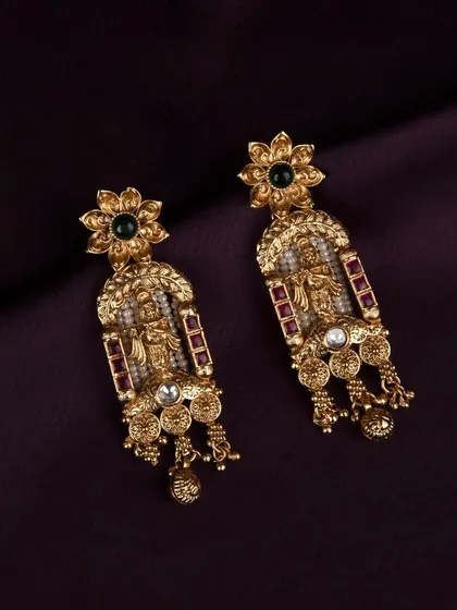 A detailed product shot of the traditional gold earrings, showcasing the intricate design with deity figures, rubies, and pearls against a dark purple background.