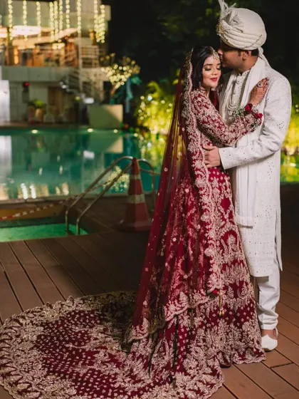 A breathtaking shot of the bride in her red gown with a long, dramatic trail, posing by the pool with her groom.