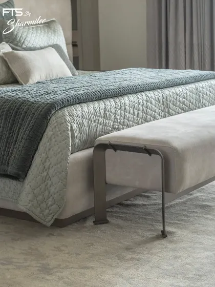A detail shot of a custom-upholstered bench with a sleek metal frame, placed at the foot of a bed. This piece adds a layer of texture and functionality to the bedroom, showcasing our attention to material and form.