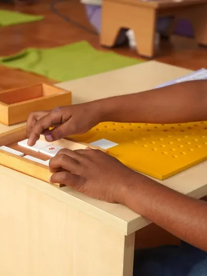 Close-up of a child's hands engaged with a language material. This tactile experience of learning letters and sounds is a core part of our literacy program, making learning to read and write a natural process.