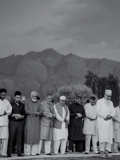 A powerful black and white photograph of the men of the family praying together against the backdrop of the mountains in Kashmir.