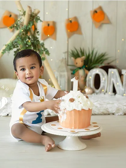 A proud moment with the birthday cake before the smashing begins. This little one is celebrating his first birthday with a cute pumpkin-themed setup.