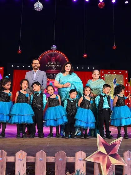 A full class of young students on stage in coordinated blue and black outfits, with sparkly vests for the boys and layered tulle skirts for the girls.