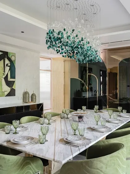 We designed this dining room as a central gathering place for celebration. The long marble dining table is surrounded by bespoke chairs upholstered in a rich green velvet, creating a sense of occasion. Overhead, a sculptural chandelier composed of green and clear glass pieces acts as a floating artwork, tying the entire space together.