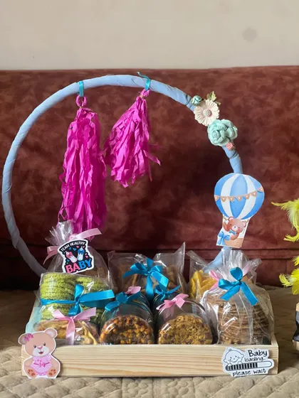 This baby shower hamper is designed as a playful mobile. It holds individually wrapped jars of snacks and treats, decorated with pink and blue ribbons to fit a gender-neutral or reveal party theme.