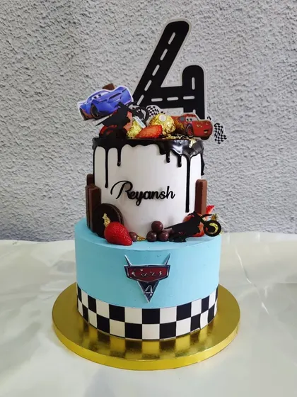 A two-tier cake for a car and bike lover. The design includes a road-shaped number 4, checkered flag details, and various vehicle toppers.