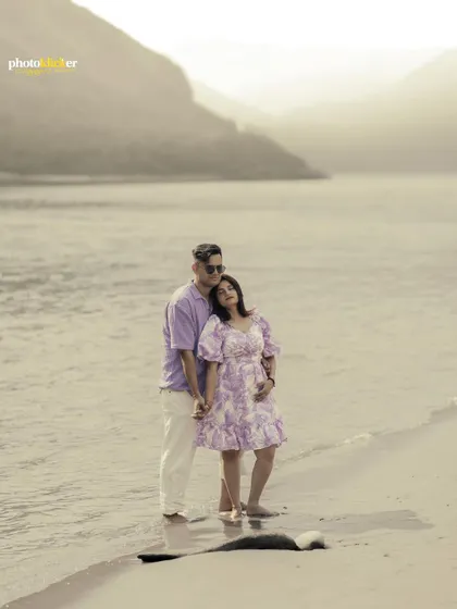 A beautifully composed portrait of a couple standing by the water's edge, with a soft, hazy light creating a dreamy atmosphere.