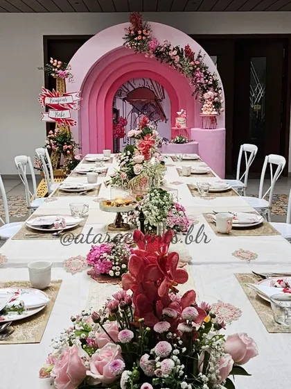 A long table setup for a Paris-themed baby shower. The table is beautifully decorated with floral runners and themed place settings, all leading to a stunning pink-arched backdrop.