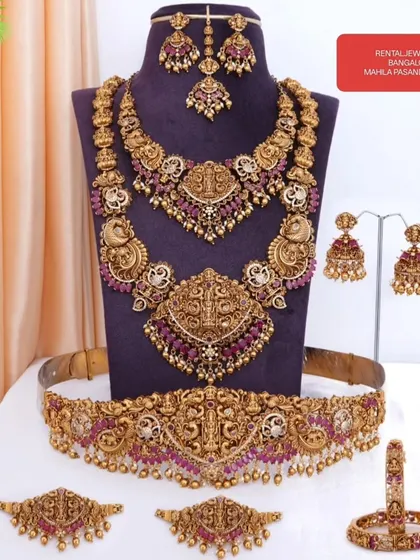 Here is a full bridal set laid out so you can see every beautiful piece. This ruby-studded temple jewellery set includes a choker, haram, vaddanam (waist belt), vanki (armlets), jhumkas, and a maang tikka. Everything you need for a complete bridal look is right here.
