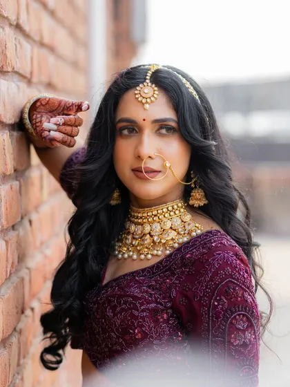 A stunning portrait of the bride against a brick wall. Her traditional jewelry and elegant pose create a timeless and beautiful image.