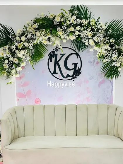 A chic and minimalist stage setup. The white sofa is framed by a beautiful arch of white flowers and tropical leaves, with a custom monogram adding a personal touch.