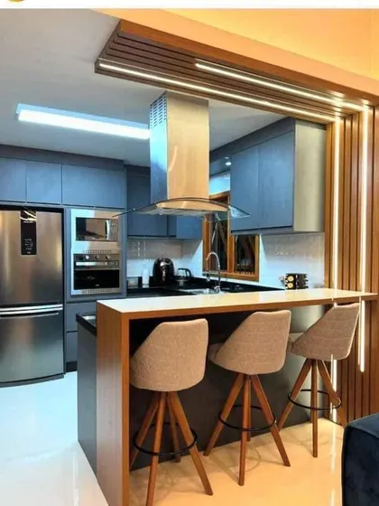 This kitchen features a breakfast bar with comfortable seating, perfect for casual meals. The grey cabinets and stainless steel chimney create a modern, semi-industrial vibe.