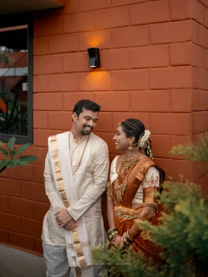 A candid shot of the couple sharing a smile against a modern, rustic wall, blending tradition with contemporary style.