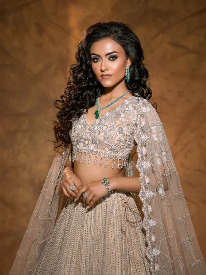 A three-quarter shot that beautifully captures the movement of the cape-like sleeves and the intricate detailing of this ethereal beige lehenga.