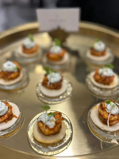 A close-up of our Harissa Prawns served on mini blinis with a dollop of cream. This bite combines spicy and creamy flavors, making it a sophisticated and popular choice for any event.