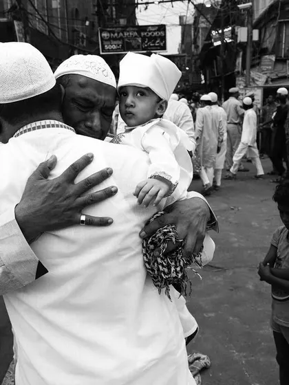 A tender moment between a father and son during Eid, captured in a crowded street. This black and white photo focuses on the intimate emotion amidst the chaos.
