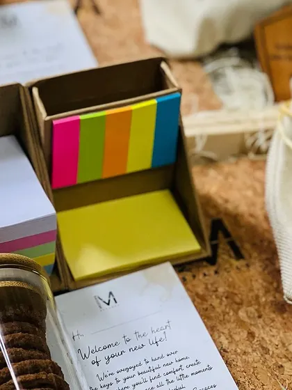 A detailed look inside a corporate hamper, showing practical desk items like sticky notes and notepads alongside cookies and a personalized welcome letter.