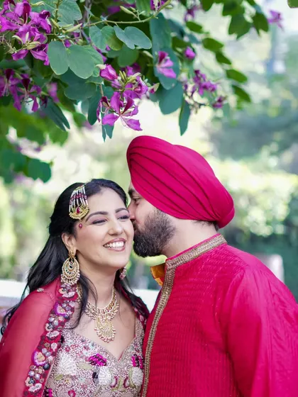 A sweet, candid moment where the groom kisses the bride's cheek. Her joyful, laughing reaction is what makes this Mehndi photo so special.
