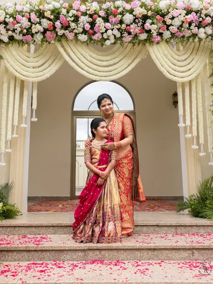 A formal portrait of a mother and daughter standing under a beautiful floral archway at the entrance of the event.