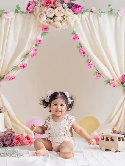A beautiful smile from the birthday girl in her floral tent. This setup, complete with a cake and soft flowers, is perfect for a classic and elegant first birthday photoshoot for a baby girl.