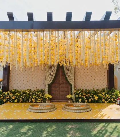 The main stage for the Haldi ceremony in Jodhpur, featuring a wooden pergola draped with strings of yellow and white flowers.