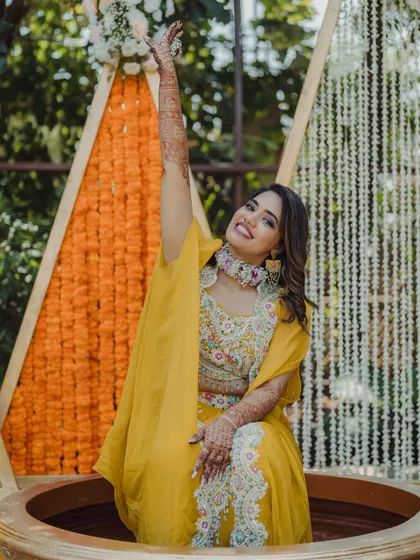 A bride celebrates during her Haldi ceremony, seated inside a large traditional vessel, a fun element we can incorporate.