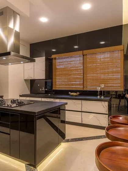 Another angle of the island kitchen, highlighting the glossy black pantry unit and the contrast with the white marble-finish cabinets.