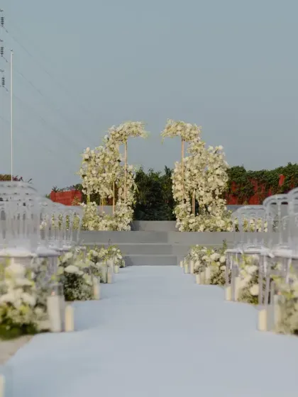 The aisle is set. A modern and chic setup with clear ghost chairs and a stunning floral arch at the end, waiting for the ceremony to begin.
